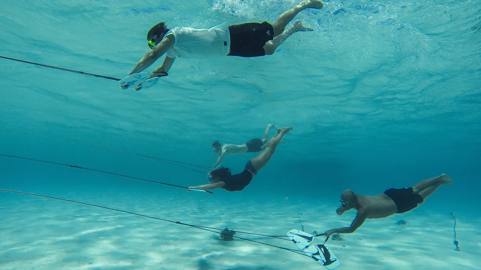 Three Subwing riders towed together underwater over a sandy bottom on a charter